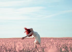 Woman with red hair in a white dress expressing freedom in a vibrant summer field.